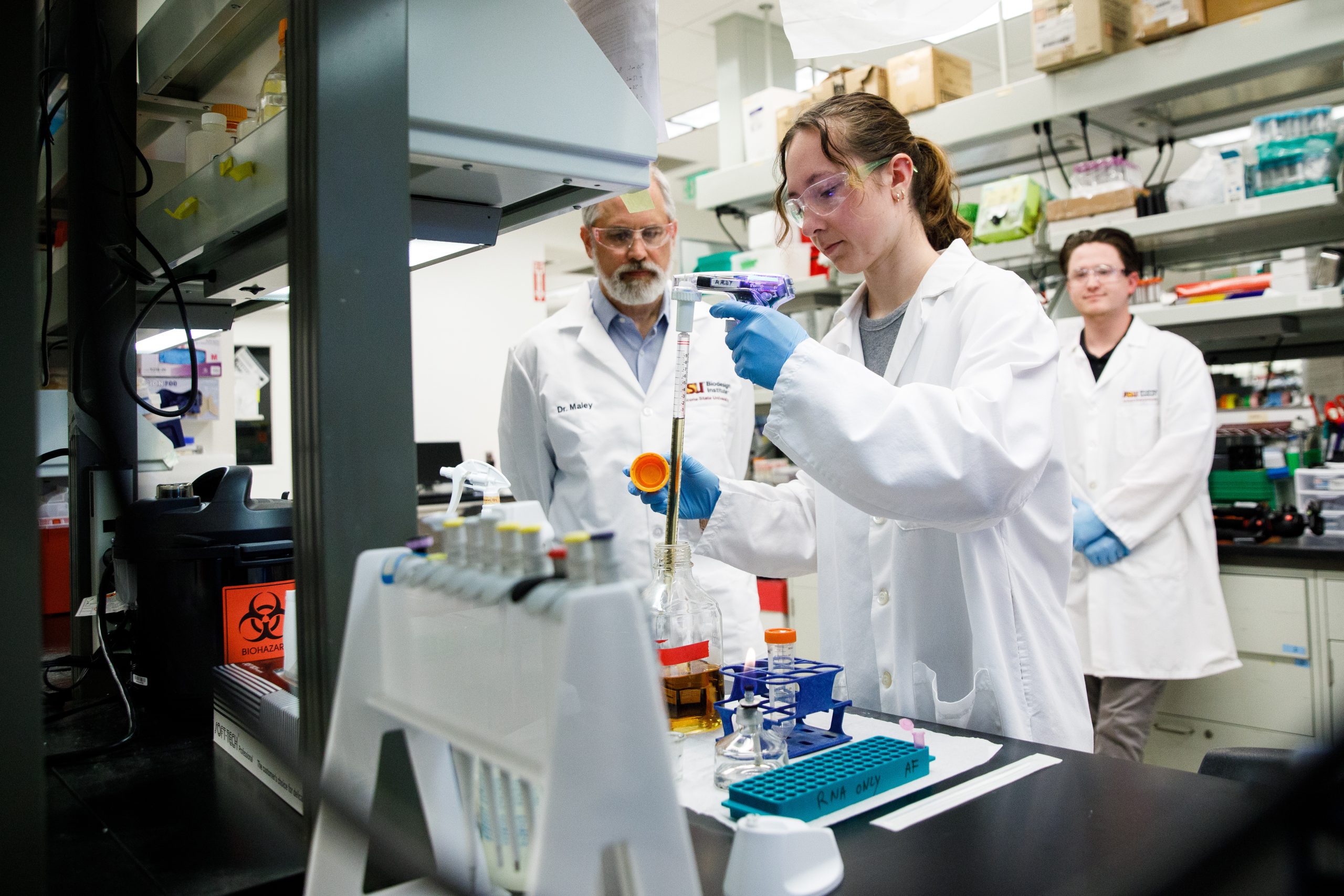Three people in white coats work in a lab