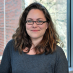 Portrait of a woman with medium length brown hair wearing glasses and a gray blouse