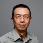 Portrait of a man with short black hair wearing glasses and a gray button up shirt